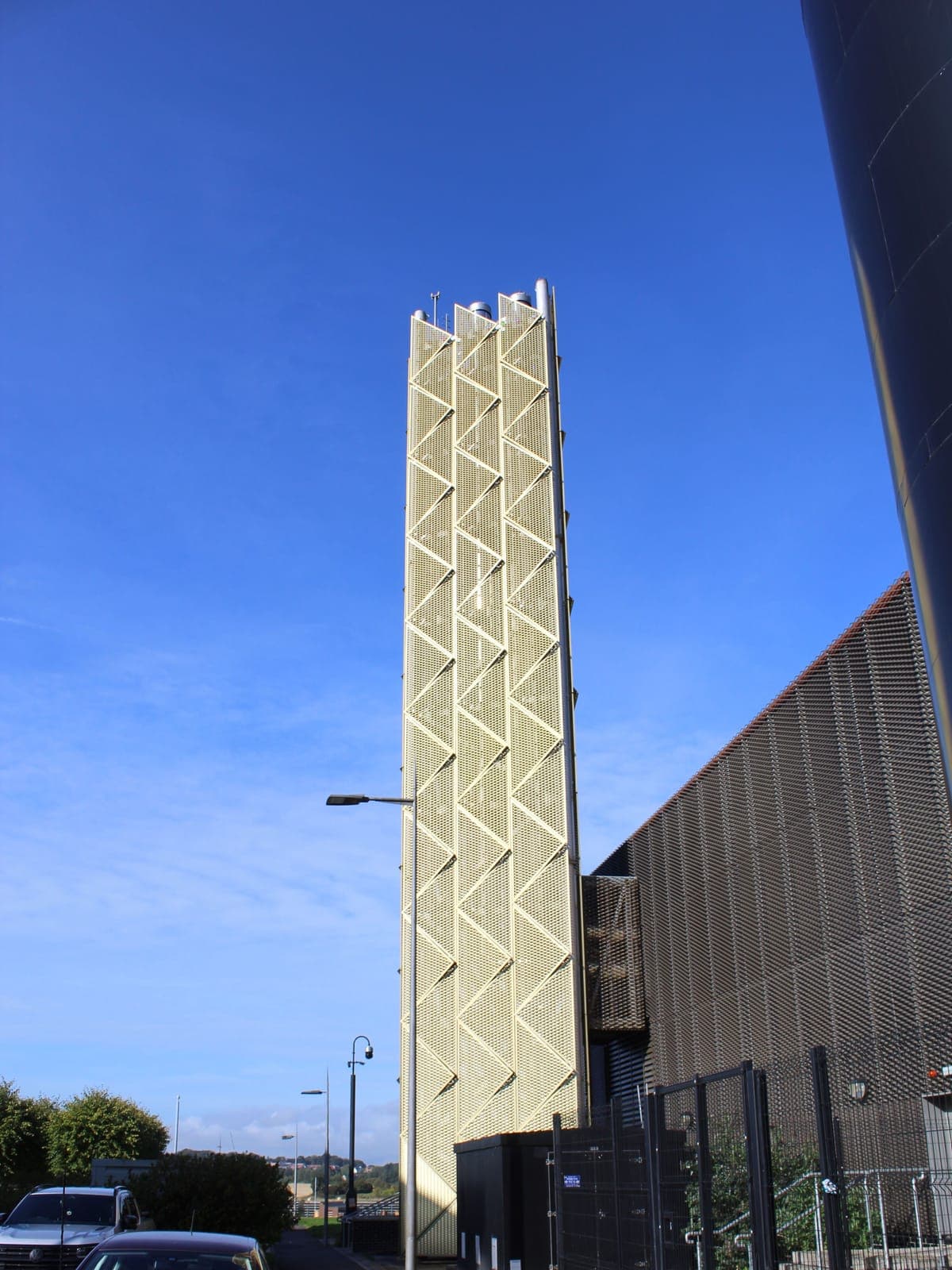 The flue tower in its expanded mesh facade, beside the dark cladding of the plant hall