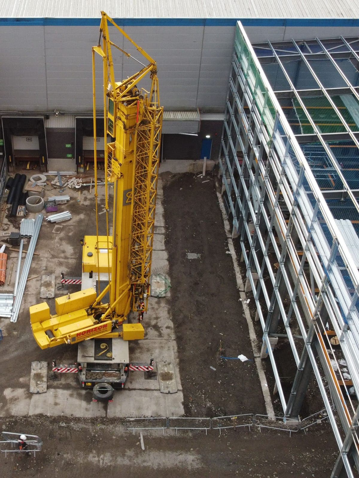 A crane beside the new steel frame, next to the existing warehouse